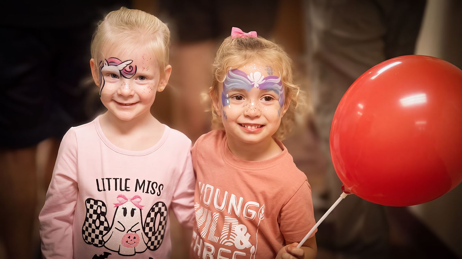 Two girls with face paint and a red balloon at the Fall Festival